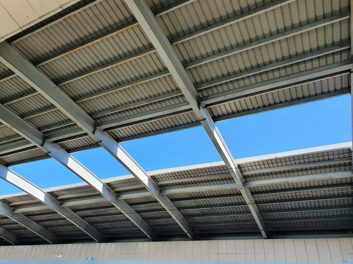 Modern roof with corrugated metal and gray steel beams against blue sky.